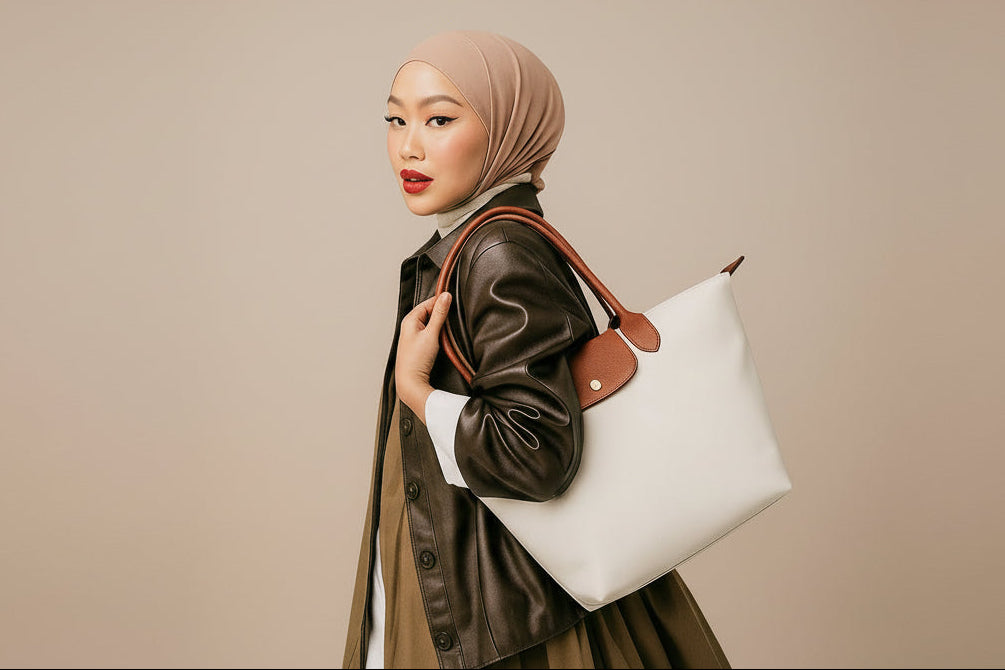 Woman holding a white handbag with a brown leather strap, wearing a hijab, on a plain background with 'ZYHA' branding.